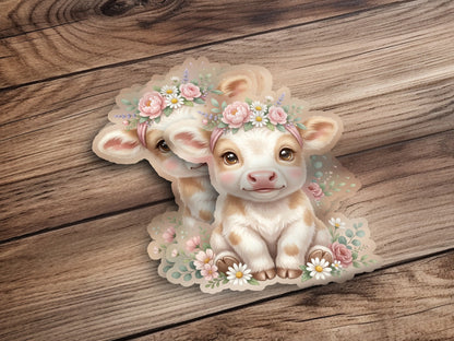 Two cute cartoon calves wearing floral crowns sit on a wooden background.
