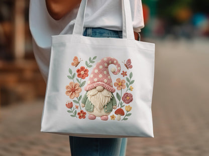 White tote bag with embroidered gnome, flowers, mushrooms, and butterflies.