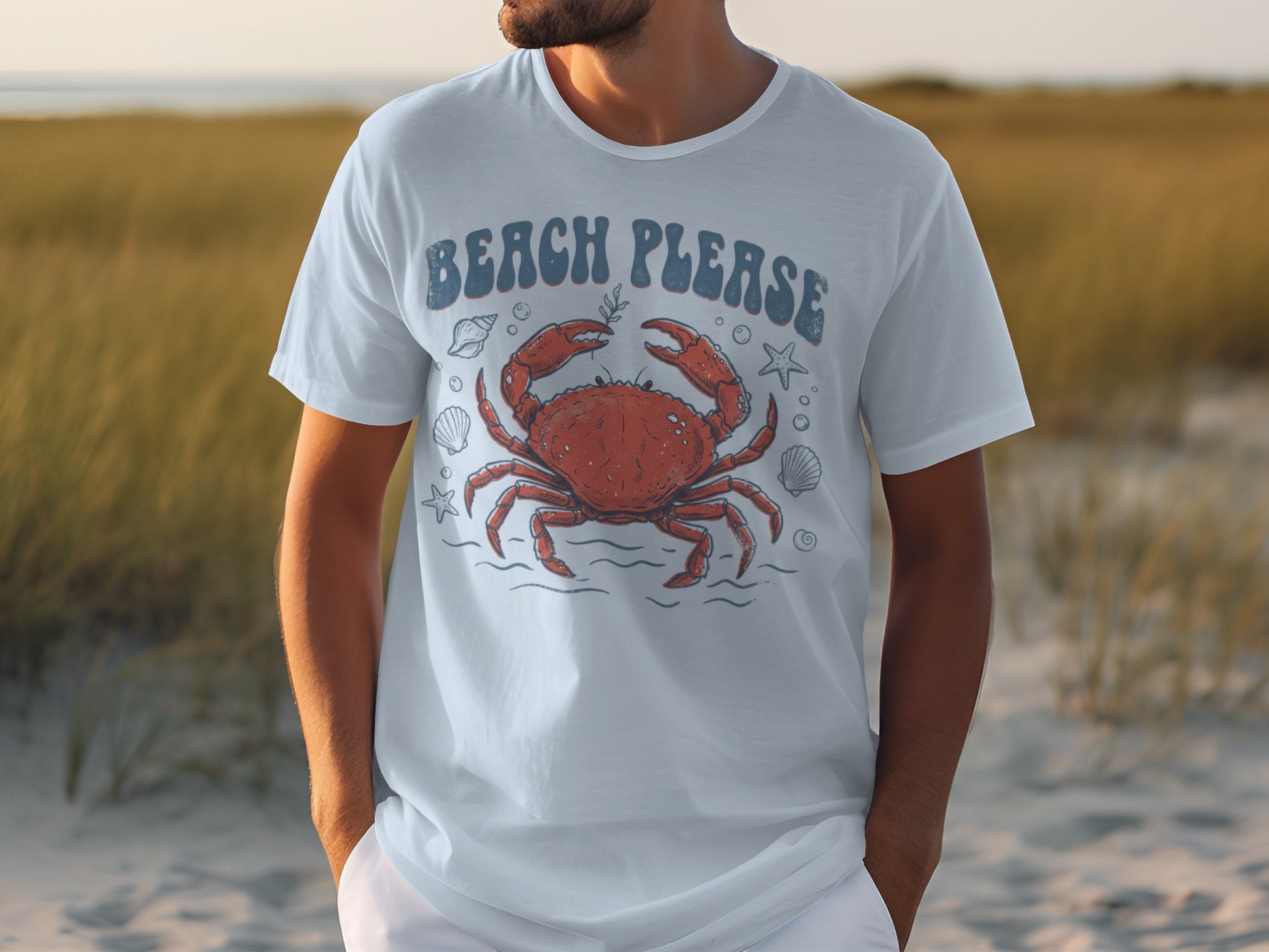 White t-shirt with crab and "Beach Please" graphic on a beach.