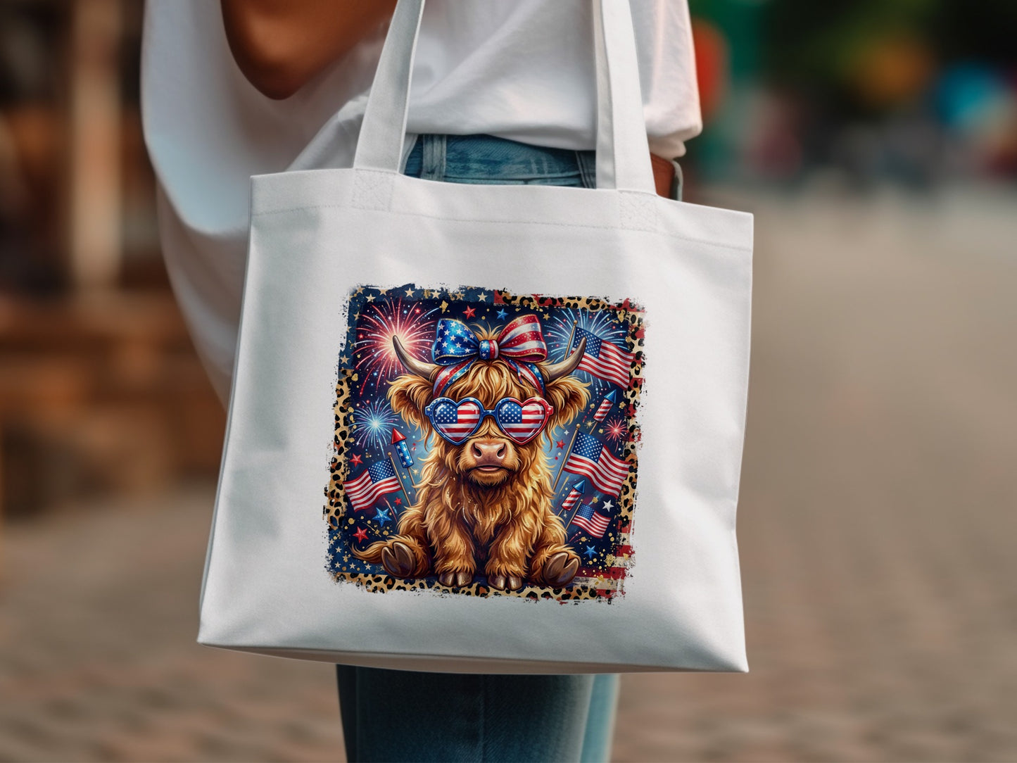 Highland cow wearing sunglasses with American flag pattern and fireworks, on white tote bag.