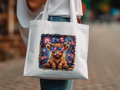 Highland cow wearing sunglasses with American flag pattern and fireworks, on white tote bag.