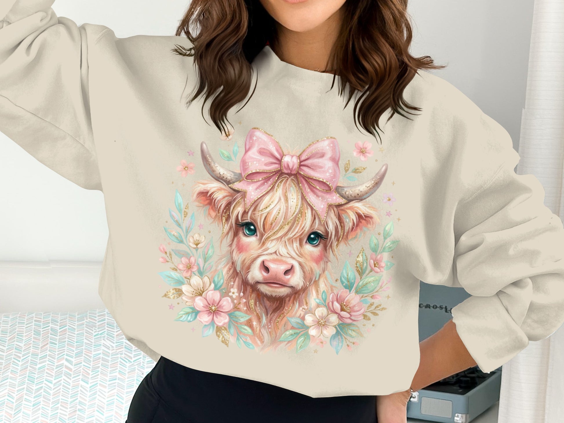 Cow illustration with pink bow and floral accents on a cream sweatshirt.