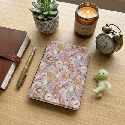 Floral e-reader cover with birds and nests, next to a notebook and candle.