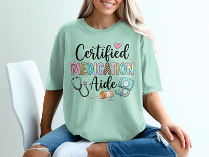 Mint t-shirt with "Certified Medication Aide" text and medical icons.