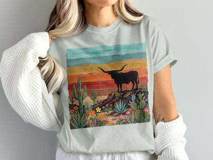 Longhorn bull silhouetted against a colorful desert sunset with cacti and wildflowers.