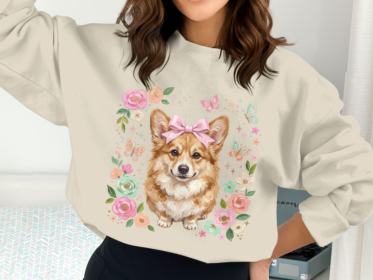 Cream sweatshirt with a Pembroke Welsh Corgi wearing a pink bow, surrounded by flowers.