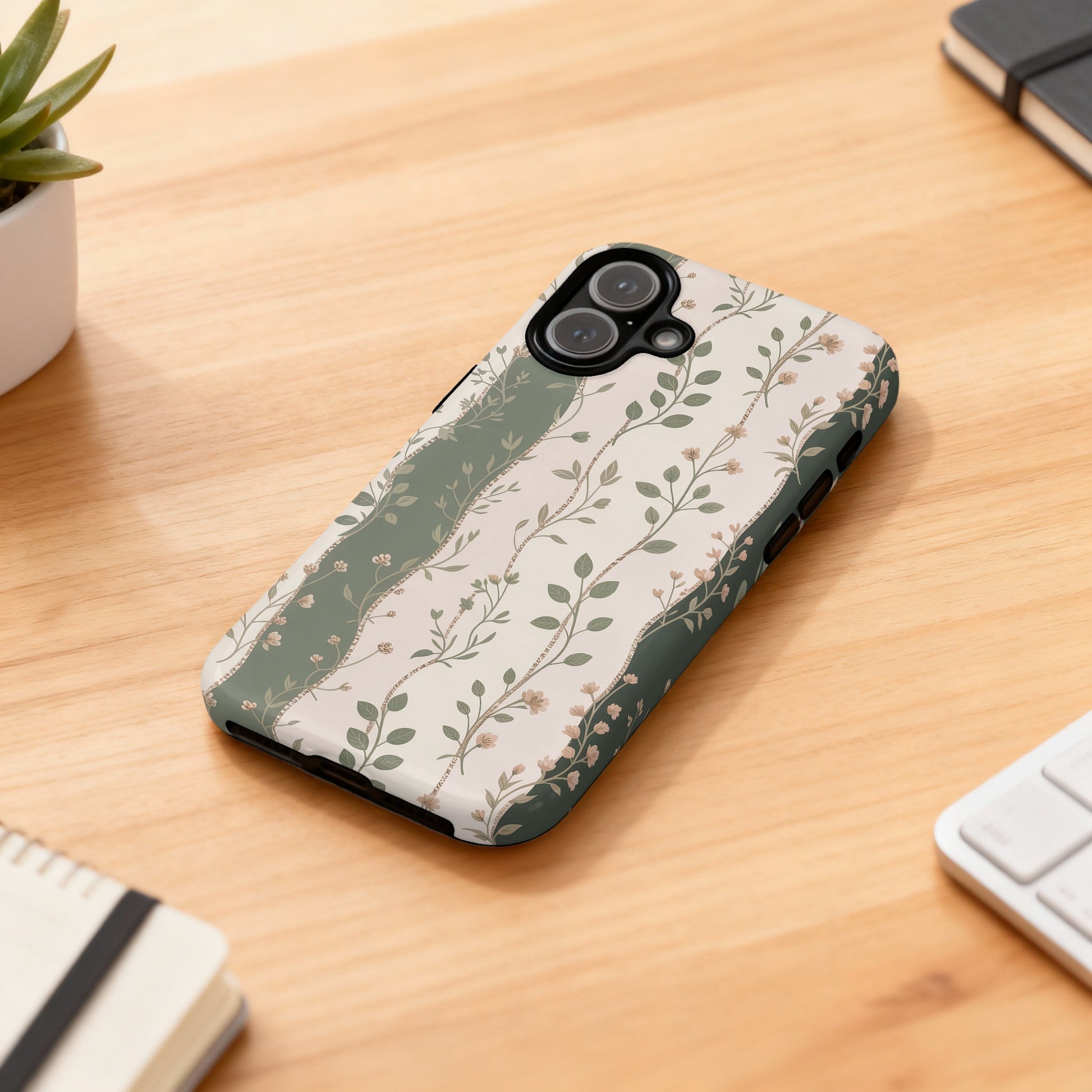 Floral vine pattern iPhone case on a wooden desk with notebooks.