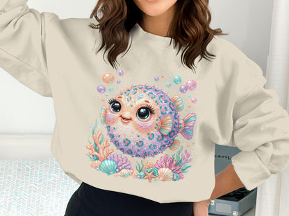 Cute pufferfish illustration with coral and seashells on a beige sweatshirt.
