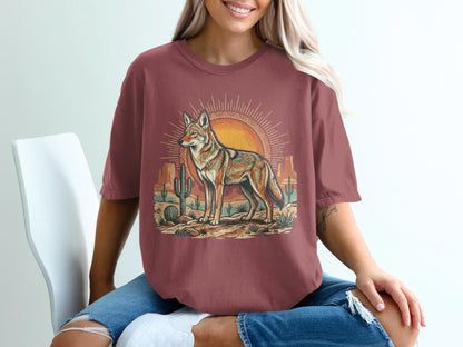 Coyote in desert landscape with sunburst and cacti, printed on maroon t-shirt.