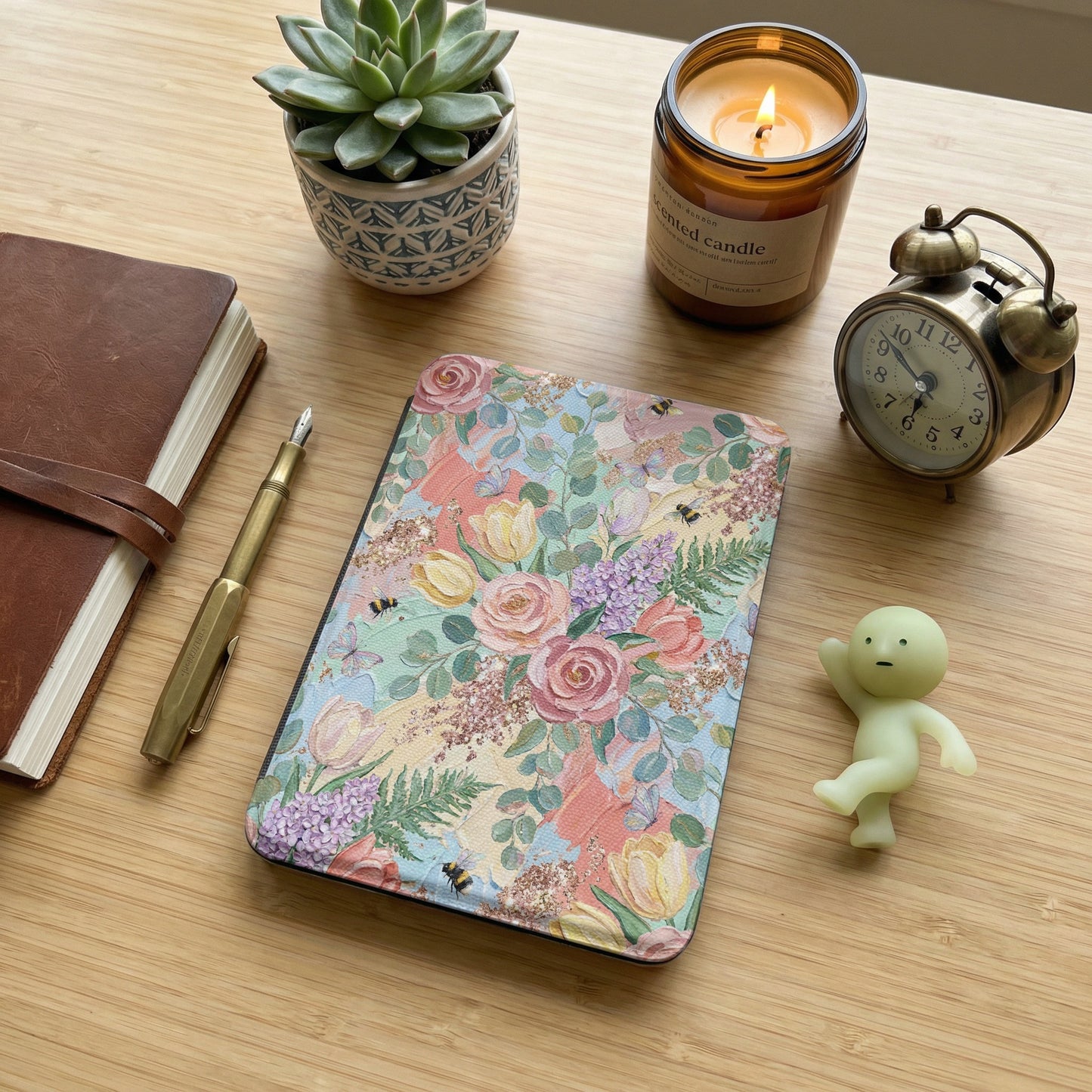Floral Kindle Scribe cover on a wooden desk with candle and alarm clock.