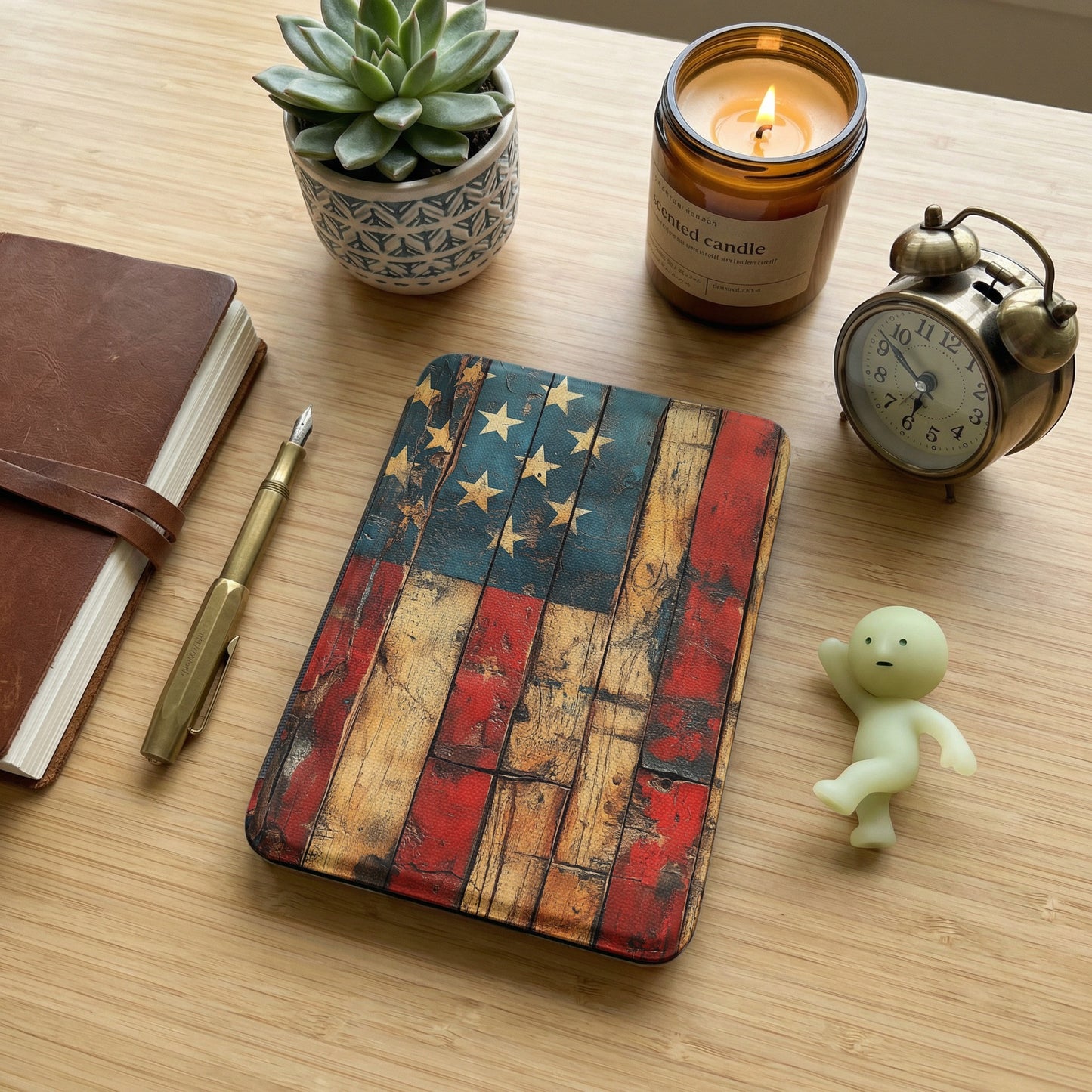 Journal, pen, American flag notebook, candle, and clock on a wooden desk.