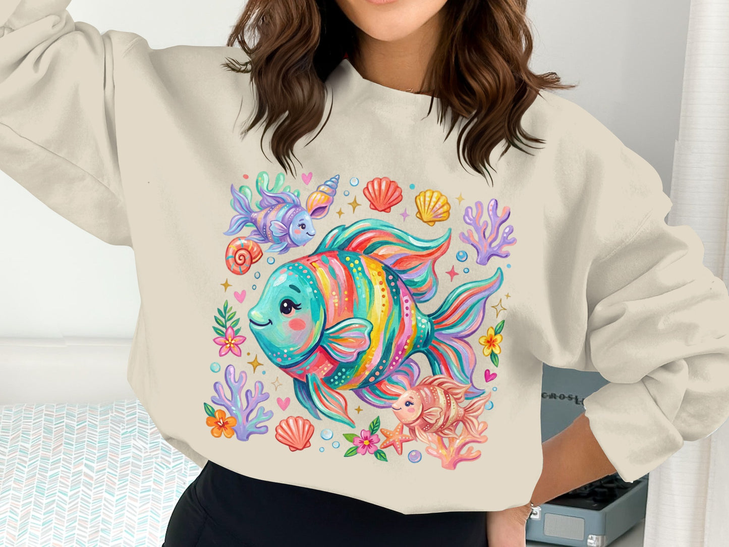 Colorful cartoon fish, shells, and sea anemones illustration on a cream sweatshirt.