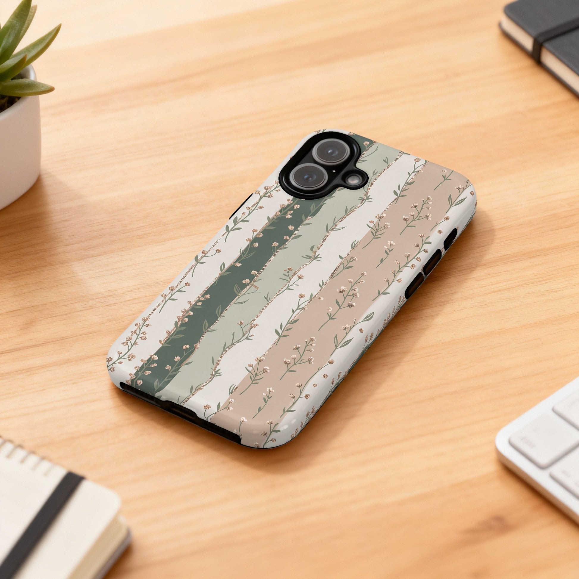 Floral patterned phone case on a wooden desk with a keyboard and notebook.