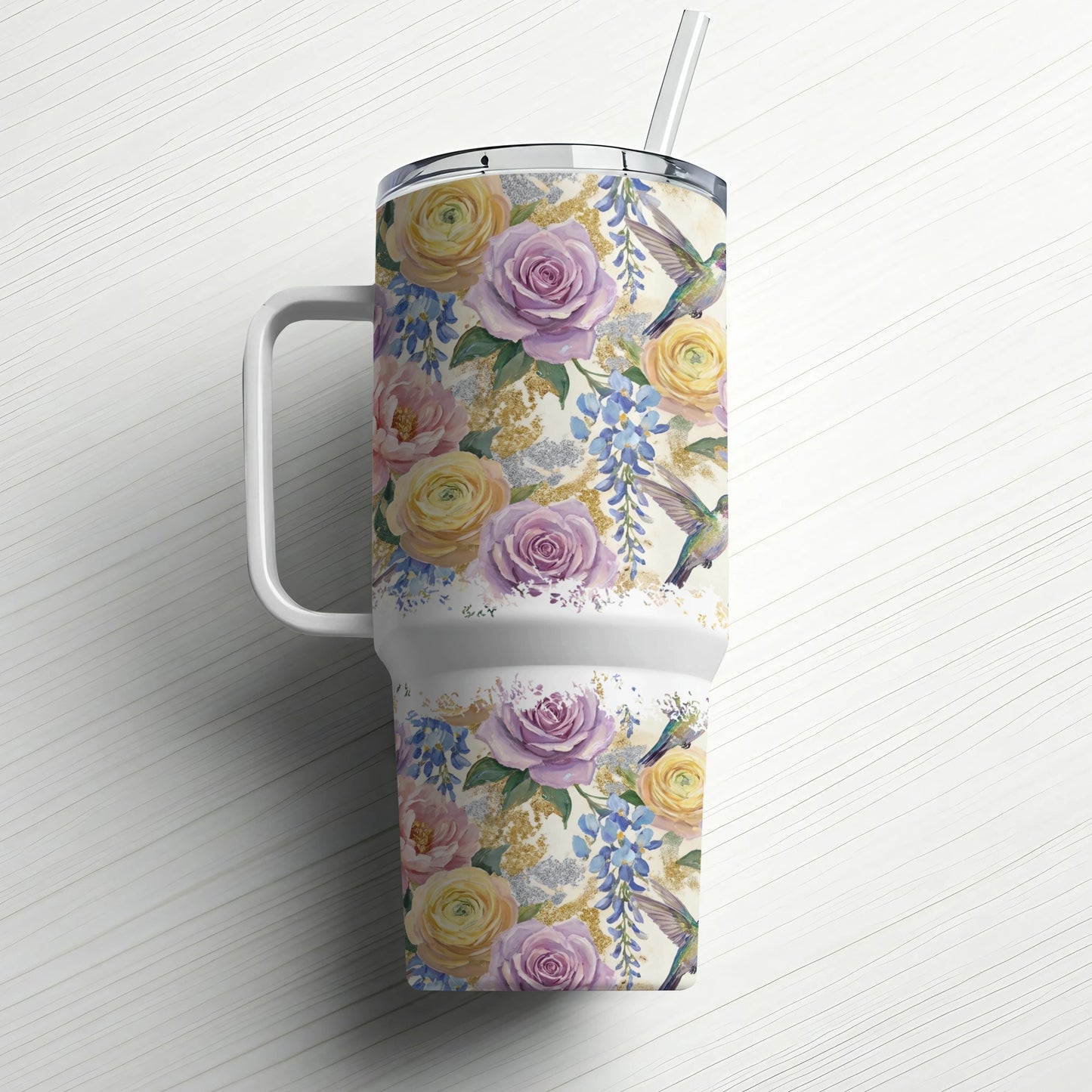 Floral tumbler with hummingbirds and a straw, against a white wooden background.