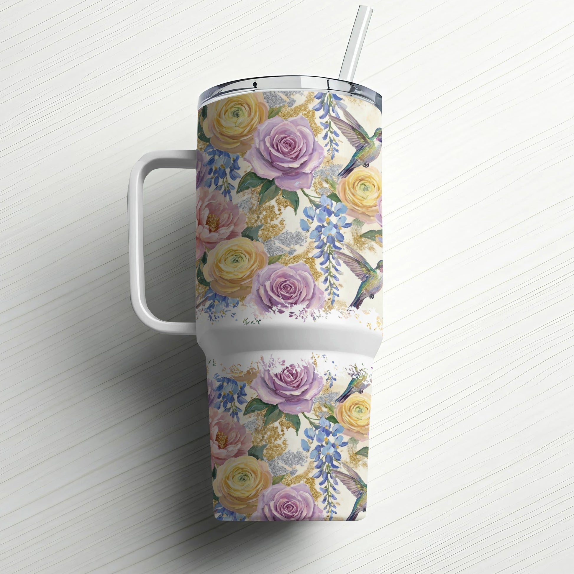 Floral tumbler with hummingbirds and a straw, against a white wooden background.