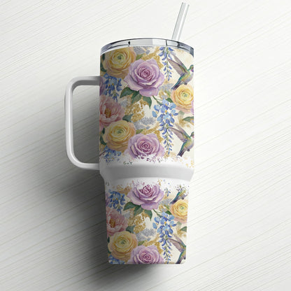 Floral tumbler with hummingbirds and a straw, against a white wooden background.