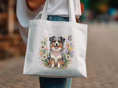 Australian Shepherd dog surrounded by flowers, butterflies, and hearts on a white tote bag.