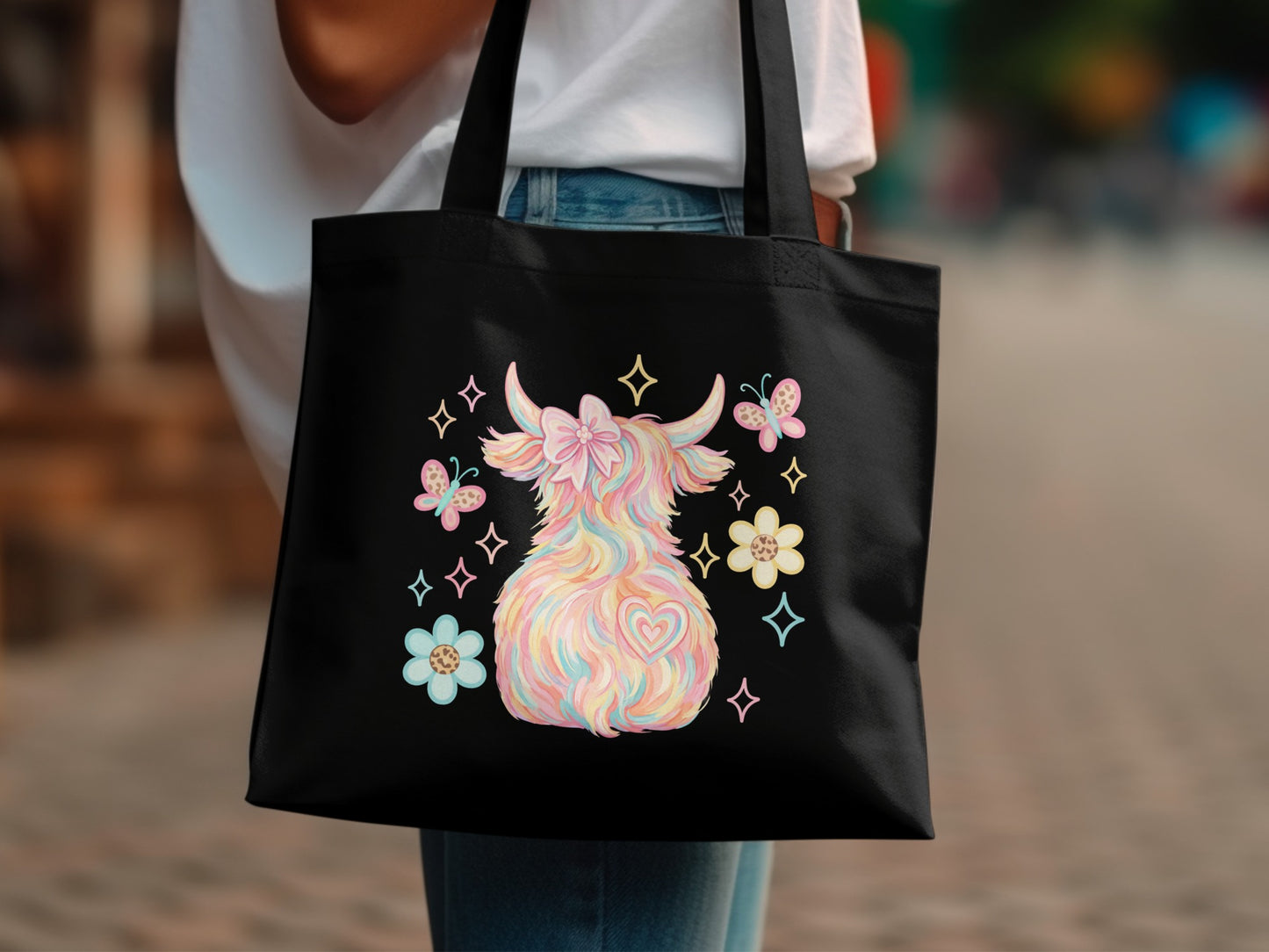 Black tote bag with pastel Highland cow, flowers, and heart design.